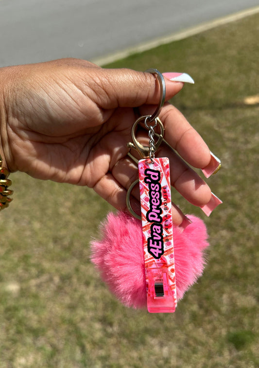 Hand holding a pink keychain with fluffy attachment against a blurred grassy background