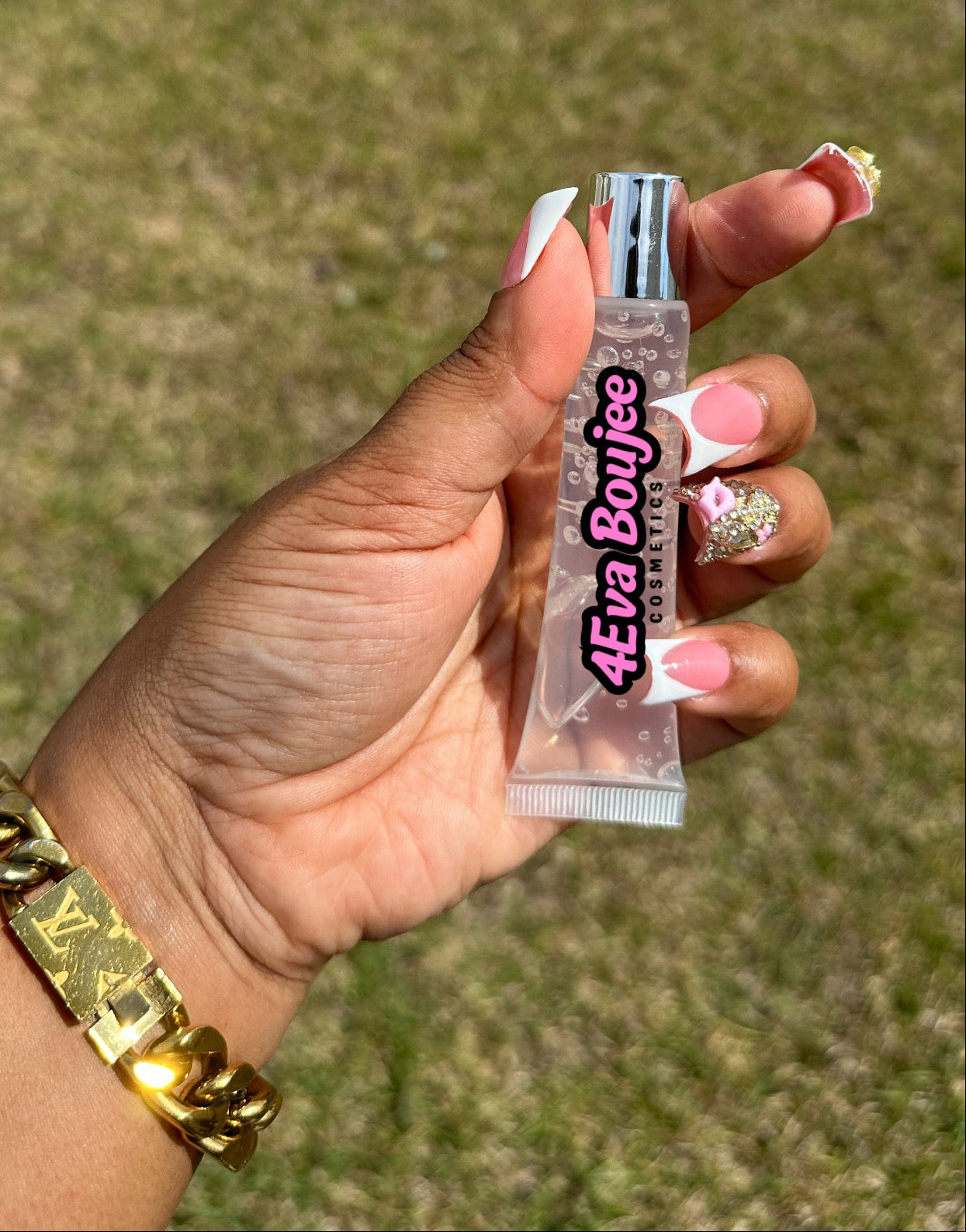 Hand holding a small bottle labeled '4eva Boujee' against a grassy background