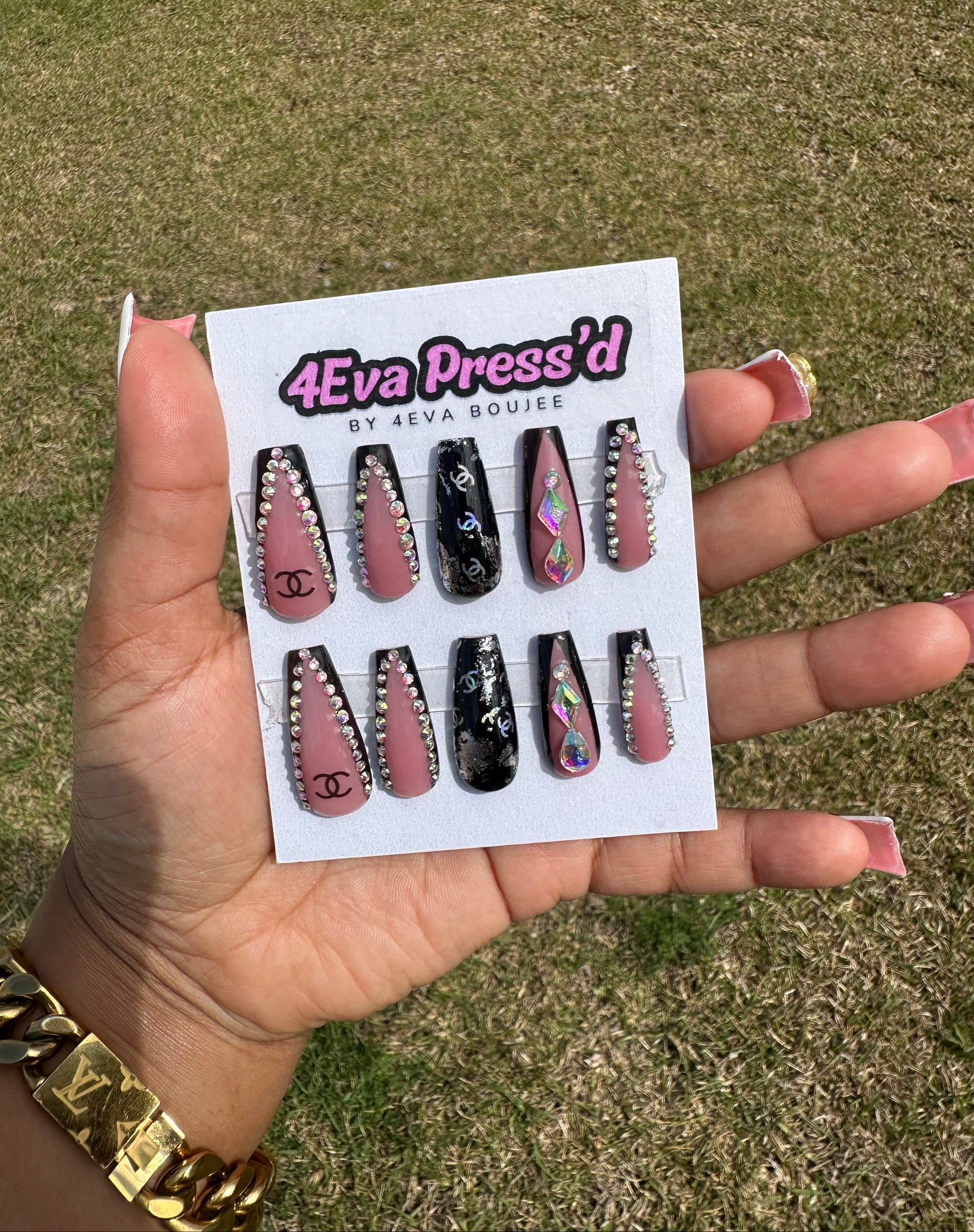 Hand holding a card with false nails labeled '4Eva Press'd' against a grassy background. 