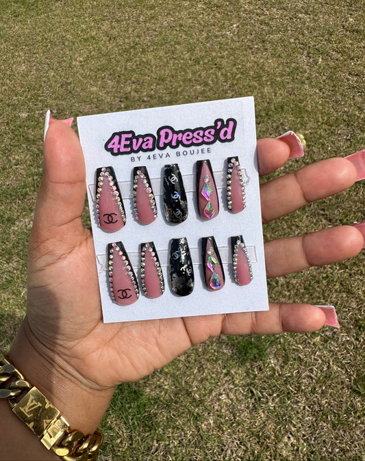 Hand holding a card with false nails labeled '4Eva Press'd' against a grassy background. 