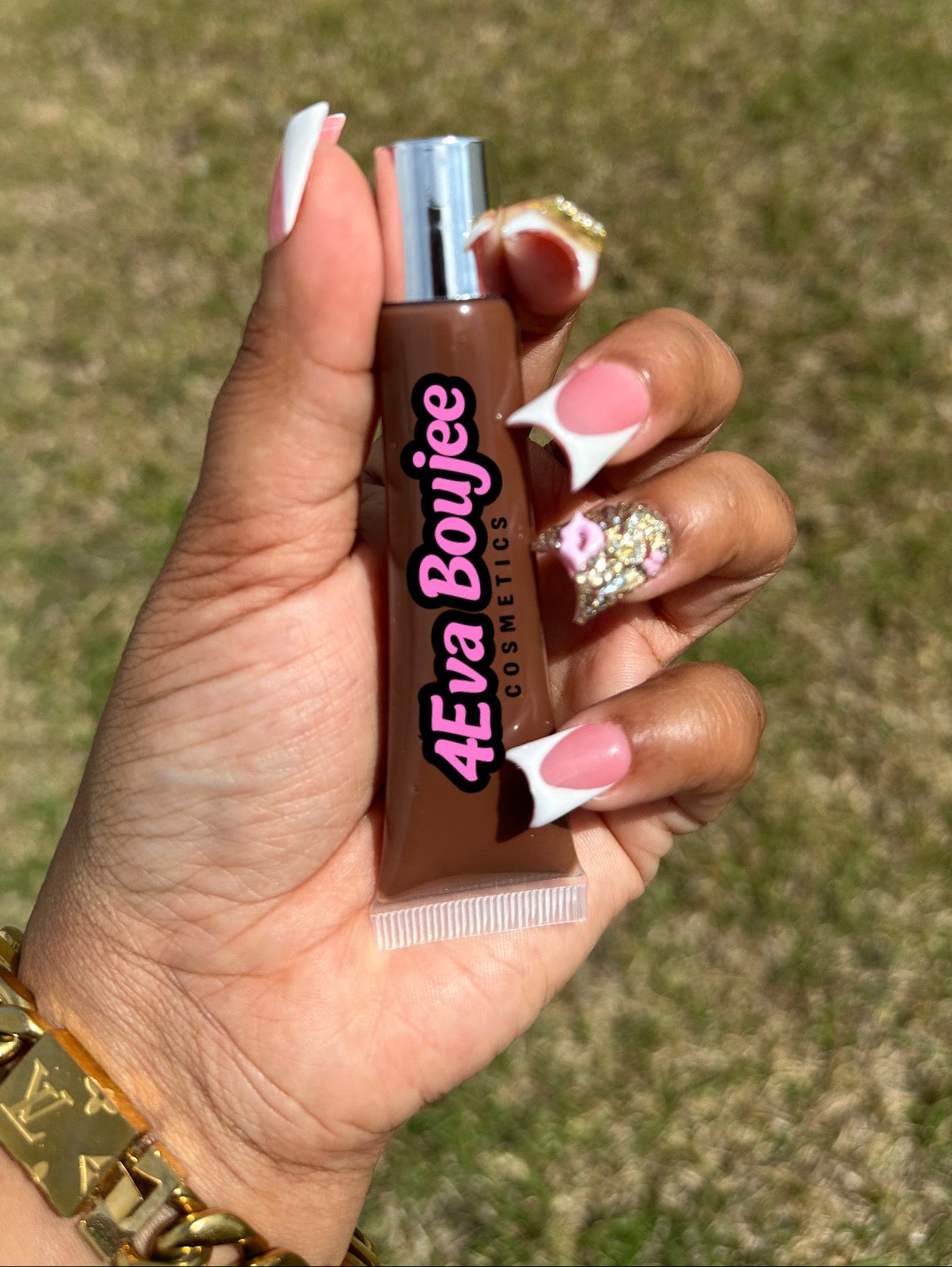 Hand holding a small bottle labeled '4eva Boujee' against a grassy background