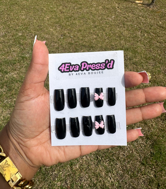 Hand holding a package of black press-on nails with pink bows against a grassy background